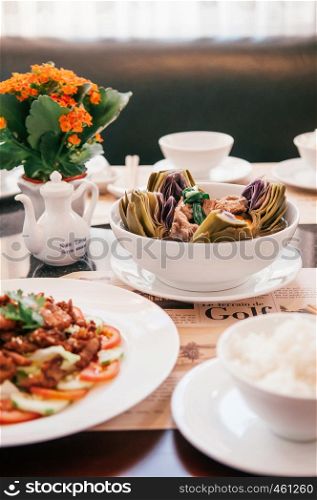 FEB 26, 2014 Dalat, Vietnam - Clear artichoke soup with pork rib and fried pork dish with rice in white bowl on newspaper designed dish mat. Vietnamese cuisine luch set in good restaurant