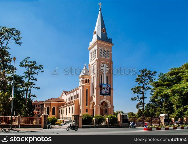 FEB 26, 2014 Dalat, Vietnam - Da Lat Cathedral yellow bell tower with local motorcycle traffic running pass in front street with blue clear sky in spring season