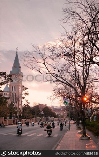FEB 26, 2014 Dalat, Vietnam - Warm sunset light and Motorcycle traffic in evening at Da Lat Cathedral with Purple orchid tree
