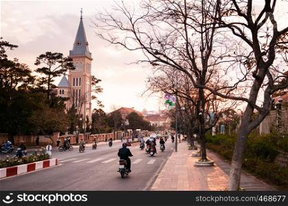 FEB 26, 2014 Dalat, Vietnam - Warm sunset light and Motorcycle traffic in evening at Da Lat Cathedral with Purple orchid tree