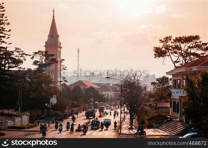 FEB 26, 2014 Dalat, Vietnam - Warm sunset light silhouette motorcycle traffic in evening at Da Lat Cathedral with Purple orchid tree