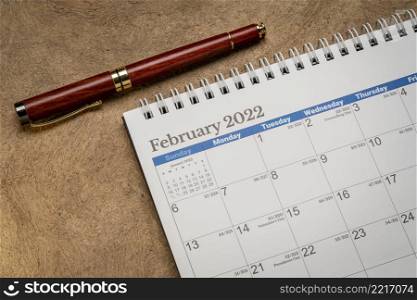 February 2022 - spiral desktop calendar against textured bark paper with a stylish pen, time and business concept
