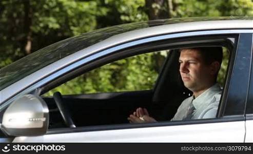 Feckless handsome driver in formal wear littering garbage from car while driving vehicle on rural road. Side view. Irresponsible man tossing crumpled napkin out of car window onto ground during road trip in countryside.