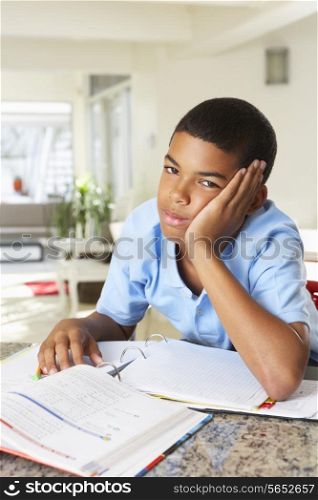 Fed Up Boy Doing Homework In Kitchen