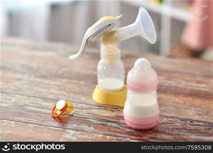 feeding concept - bottle with baby milk formula, soother and breast pump on wooden table at home. bottle with baby milk formula and breast pump