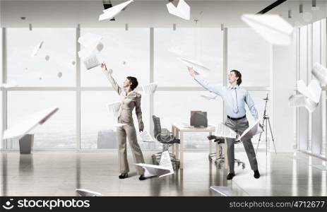 Feeling free and careless. Young businessman and businesswoman in modern office interior playing with paper plane