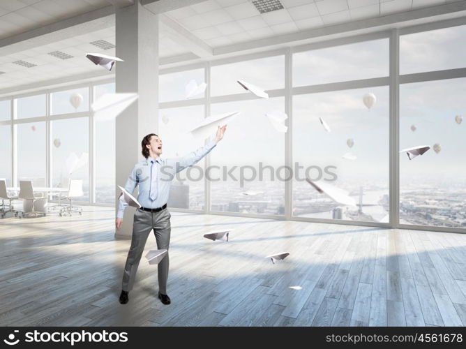 Feeling free and careless. Young businessman in modern office interior playing with paper plane