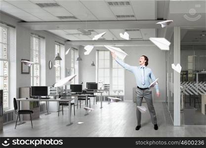 Feeling free and careless. Young businessman in modern office interior playing with paper plane