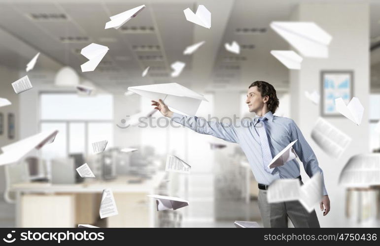 Feeling free and careless. Young businessman in modern office interior playing with paper plane