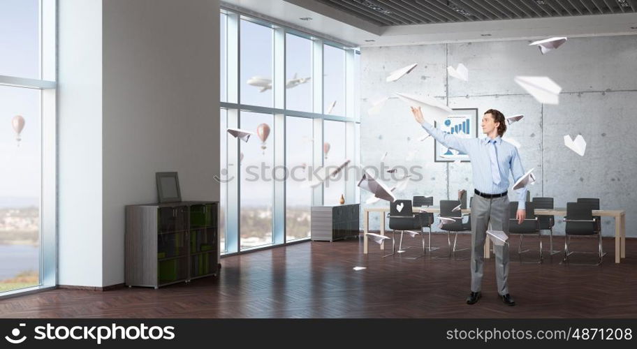Feeling free and careless. Young businessman in modern office interior playing with paper plane