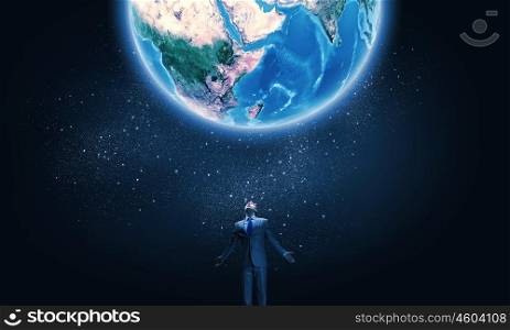 Feeling powerful. Young businessman and Earth planet above. Elements of this image are furnished by NASA