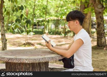 Feeling tired. Young man holding book sitting on bench in the park and keeping eyes closed