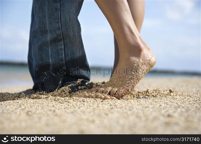 Feet and legs of mid-adult Caucasian couple standing together on beach.