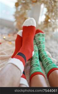 Feet in christmas socks near the Christmas tree. Couple sitting at the blanket, relaxes warming up their feet in woollen socks. Winter and Christmas holidays concept