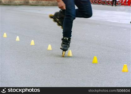 Feet of a skater while performing the slalom between yellow plastic cones placed in line on the asphalt