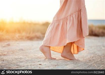 feet of a woman in a pink dress walking on the sand during sunset