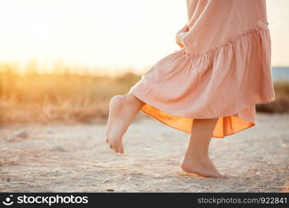 feet of a woman in a pink dress walking on the sand during sunset