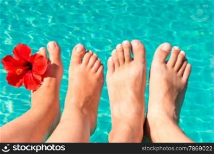 feet of a young couple by the pool with a red flower