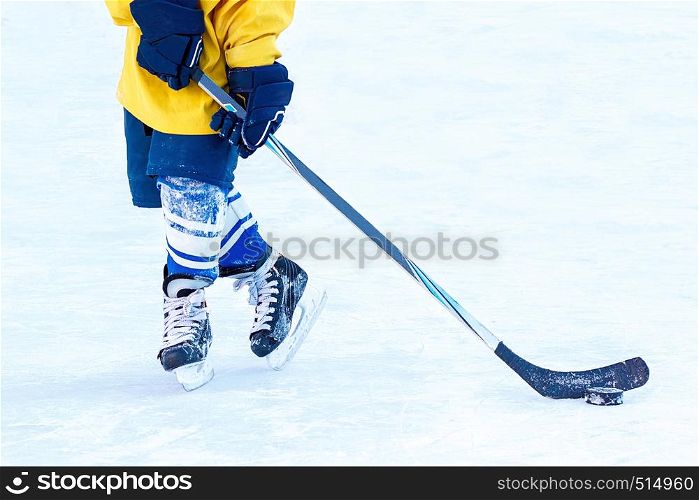 Feet of a young hockey player, hockey stick and puck close-up on the background of the ice.