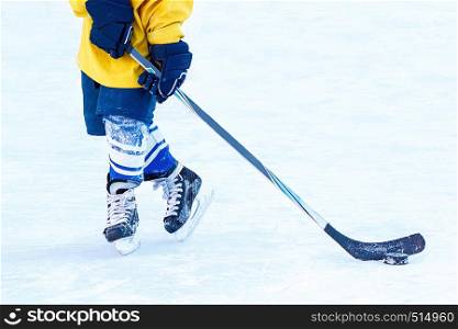 Feet of a young hockey player, hockey stick and puck close-up on the background of the ice.