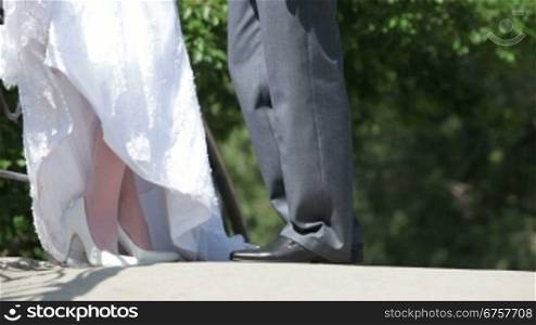 feet of bride and groom standing hugging on bridge