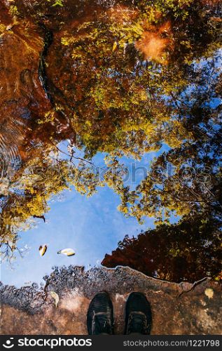Feet shot and beautiful tree leaves shadow and blue sky reflected on water surface in tropical forest at Phu Kradueng National park, Loei - Thailand