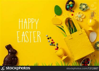Felt Easter decorations and sweets on yellow background, flat lay, copy space