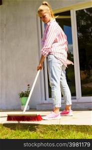 Female adult young woman using big broom to clean up backyard patio. Woman using broom to clean up backyard patio