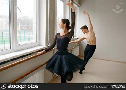Female and male ballet dancers doing exercise at barre. Ballerina with partner training in class, dance studio interior on background. Female and male ballet dancers, exercise at barre