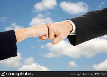 Female and male business hands doing a fist bump with sky for a background.