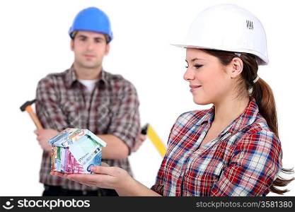 Female and male construction worker holding house made from money