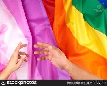 female and male hand outstretched against the background of flags of LGBT communities, concept against gender discrimination