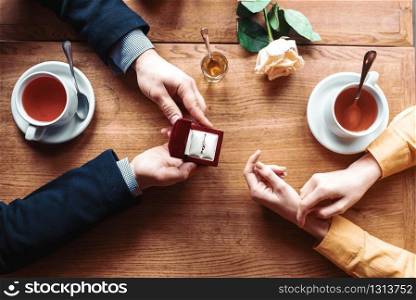 Female and male hands with wedding ring top view, wooden table, rose and cups on background. Couple romantic date. Marriage proposal