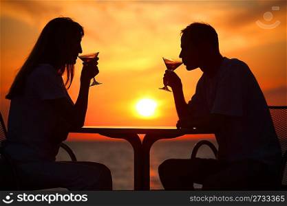Female and man&acute;s silhouettes on sunset drink from glasses