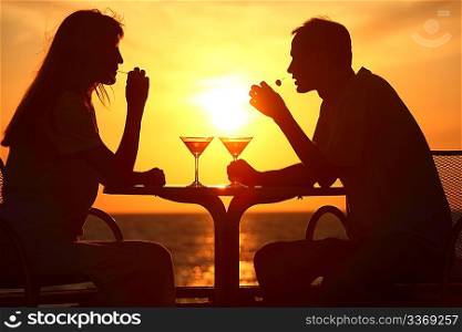 Female and man&acute;s silhouettes on sunset sit at table with two glasses and olives outdoor