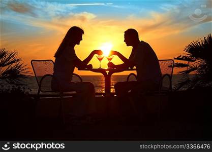 Female and man&acute;s silhouettes on sunset sit at table with two glasses outdoor