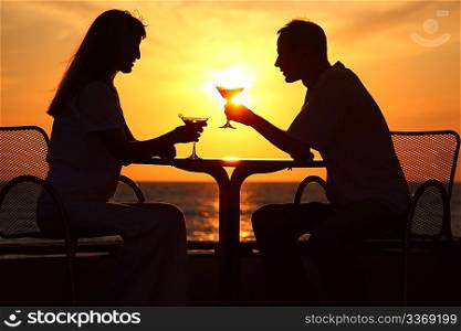 Female and man&acute;s silhouettes on sunset sit at table with two glasses outdoor