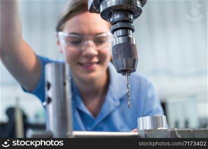 Female Apprentice Using Drill In Factory