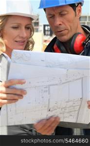 female architect and workman consulting blueprints in construction site
