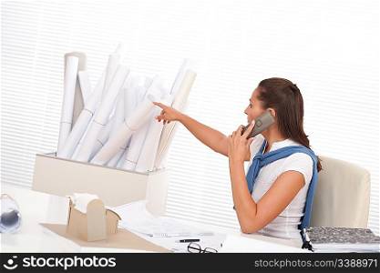 Female architect calling with phone at the office watching plans