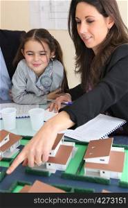 female architect in office with little girl pointing at model