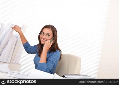 Female architect on the phone sitting at the office holding plans