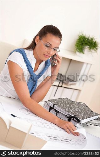Female architect with phone sitting at the office