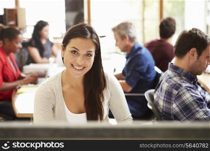 Female Architect Working At Desk With Meeting In Background