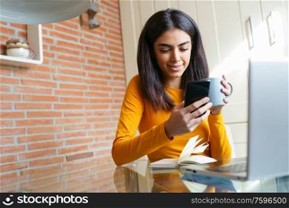 Female architect working at home with a laptop and blueprints. Persian woman. Persian woman with a coffee mug.. Female architect working at home with a laptop and blueprints