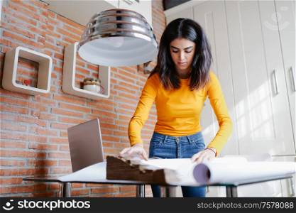 Female architect working at home with a laptop and blueprints. Persian woman designing a project.. Female architect working at home with a laptop and blueprints