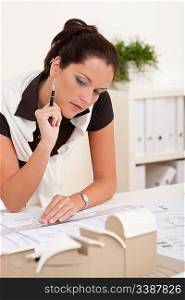 Female architect working at the office with plans and architectural model
