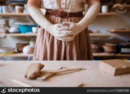 Female artisan hands covered with dried clay, pottery workshop interior on background. Woman molding a bowl. Handmade ceramic art, tableware making. Artisan hands covered with dried clay, pottery