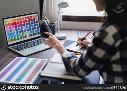 Female artist designer choosing color swatch s&les on laptop and drawing logo on graphic tablet.