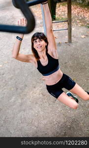 Female athlete doing monkey exercises on rings in a park. Woman doing monkey exercises on rings